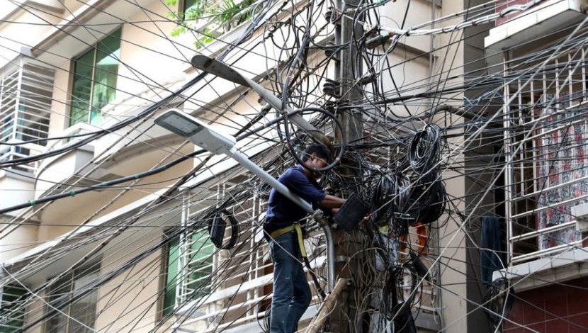 কোনোরকম সুরক্ষা ব্যবস্থা ছাড়াই বিদ্যুতের খুঁটিতে কাজ করছে স্যাটেলাইট ক্যাবল নেটওয়ার্ক কর্মীরা। রামপুরা, বনশ্রী, ঢাকা, ছবি: ইন্দ্রজিৎ কুমার ঘোষ